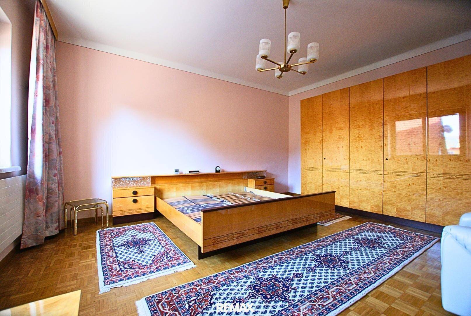 Schlafzimmer mit Parkettboden, großem Bett und Einbauschränken aus Holz.