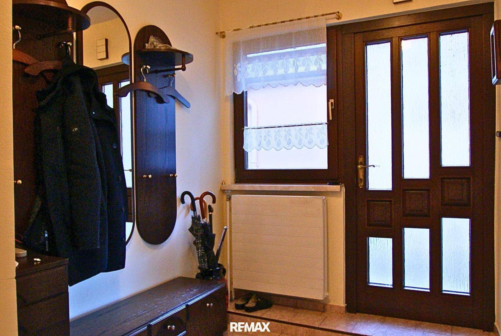 Gemütlicher Eingangsbereich mit Garderobe, Spiegel und Holztür mit Glaseinsätzen.