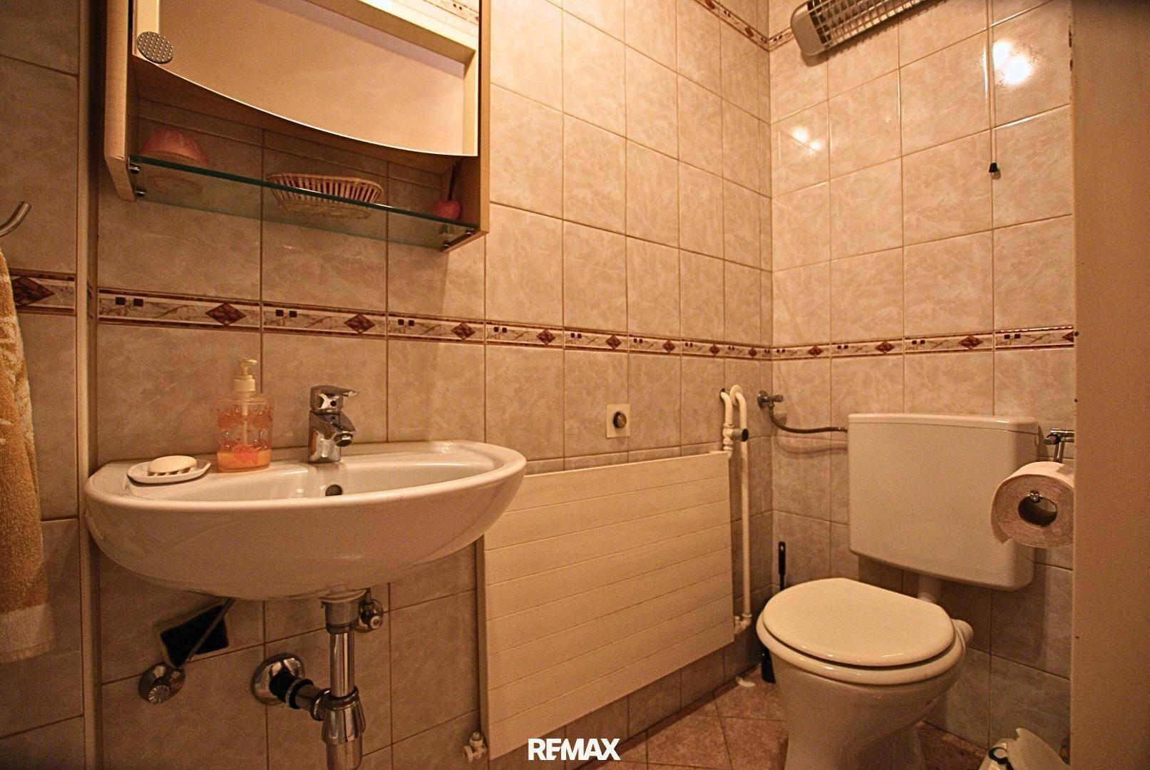 Kleines Gäste-WC mit hellen Wandfliesen, Waschbecken und Heizkörper.