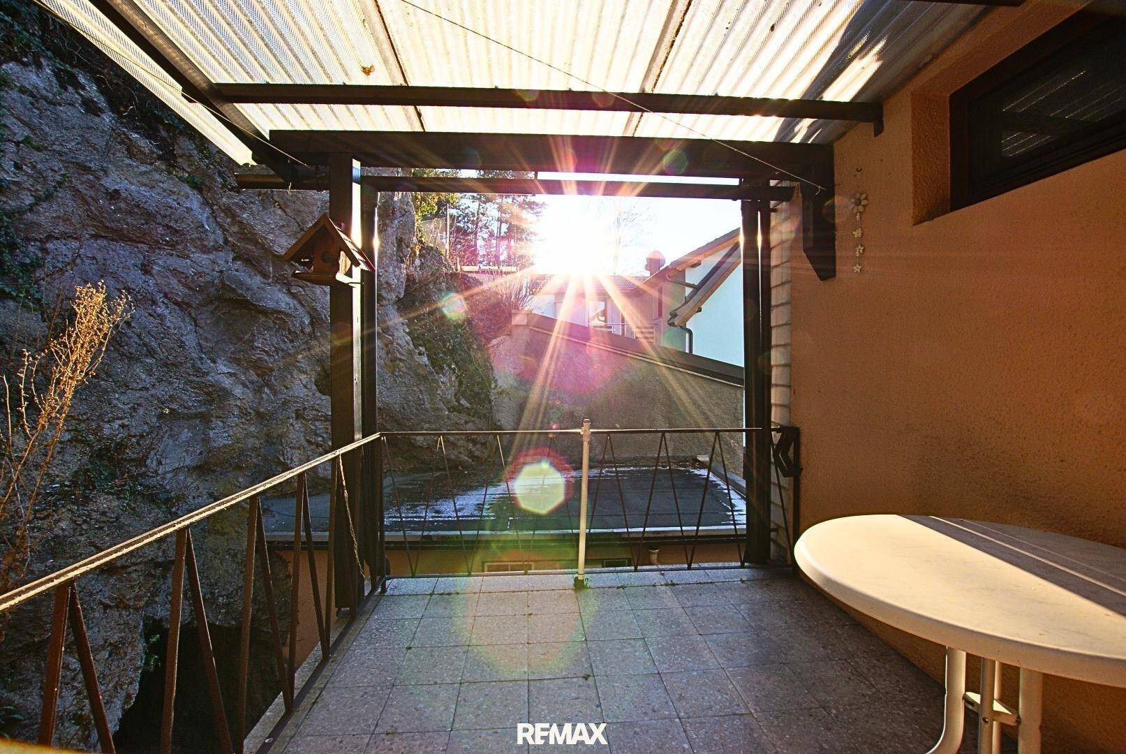Überdachte Terrasse mit Fliesenboden und Blick auf die Umgebung bei Sonnenlicht.
