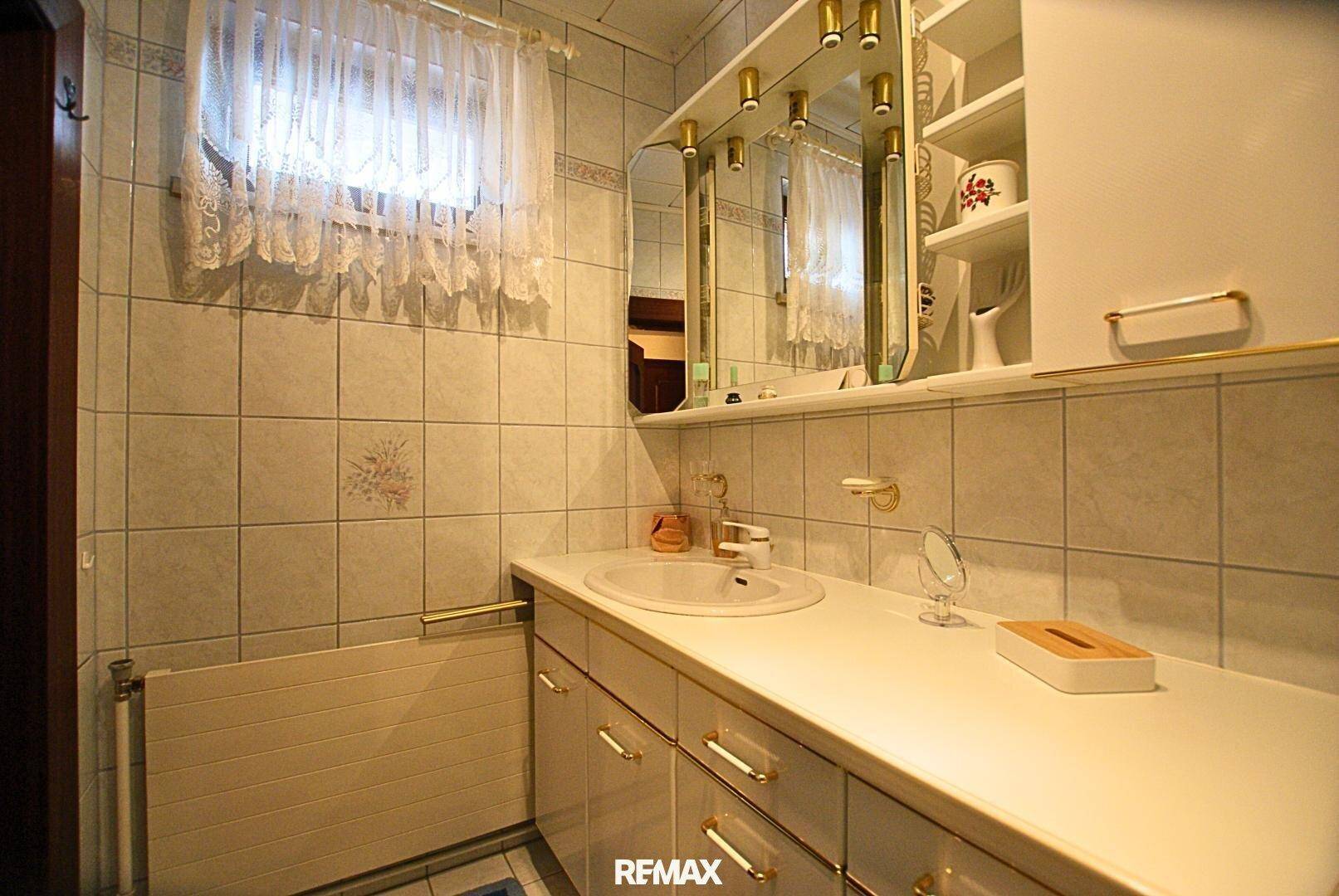 Badezimmer mit Fliesen, Waschbecken, Spiegelschrank und Fenster.