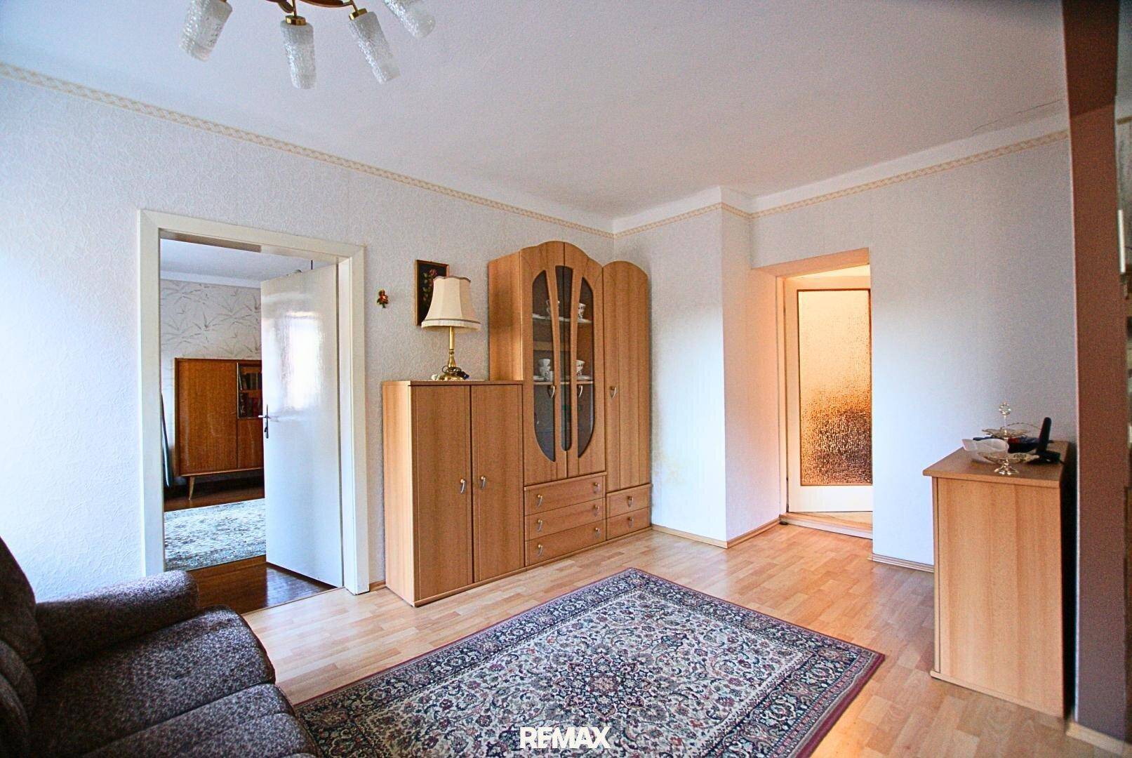 Wohnzimmer mit Parkettboden, Teppich und einem großen Holzschrank.