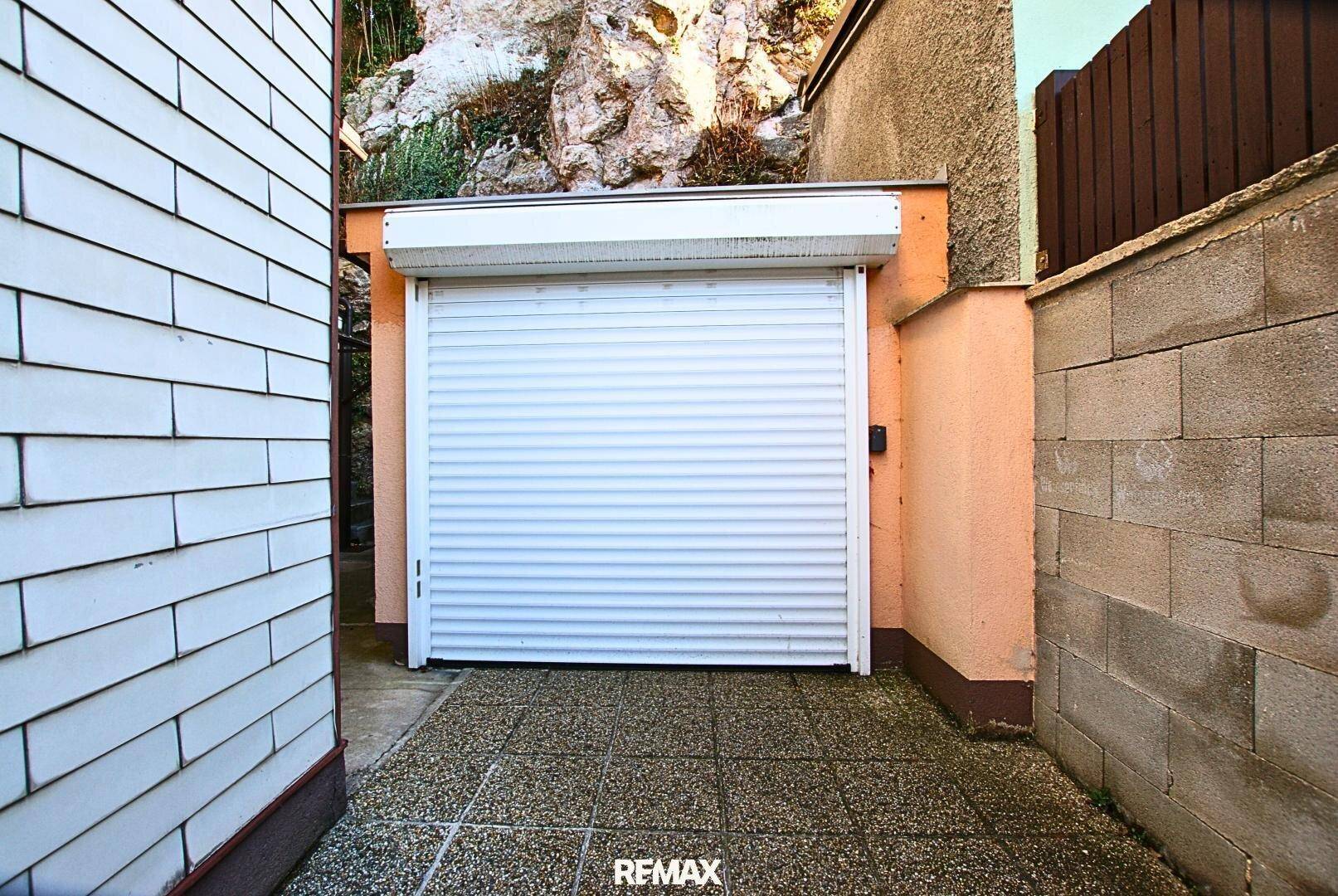 Einzelgarage mit weißem Rolltor und gepflastertem Zugang direkt am Haus.