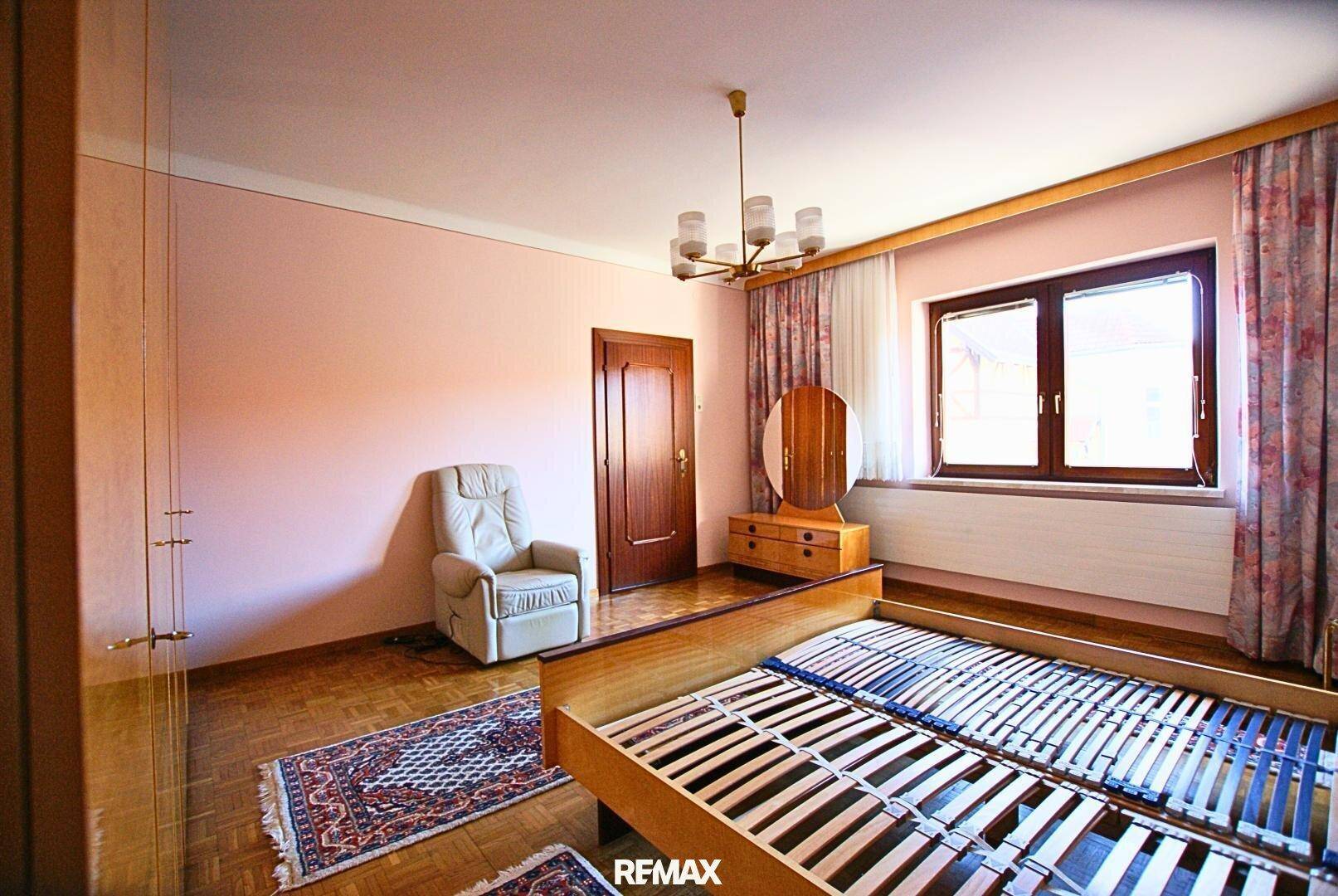 Schlafzimmer mit Doppelbett, Kleiderschrank und Fenster mit Blick ins Grüne.