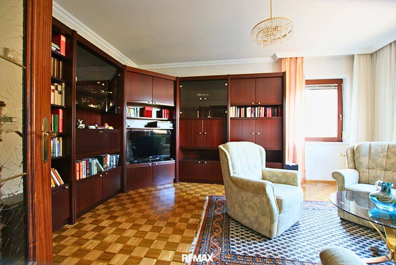 Geräumiges Wohnzimmer mit Parkettboden, großer Schrankwand und bequemen Sesseln.