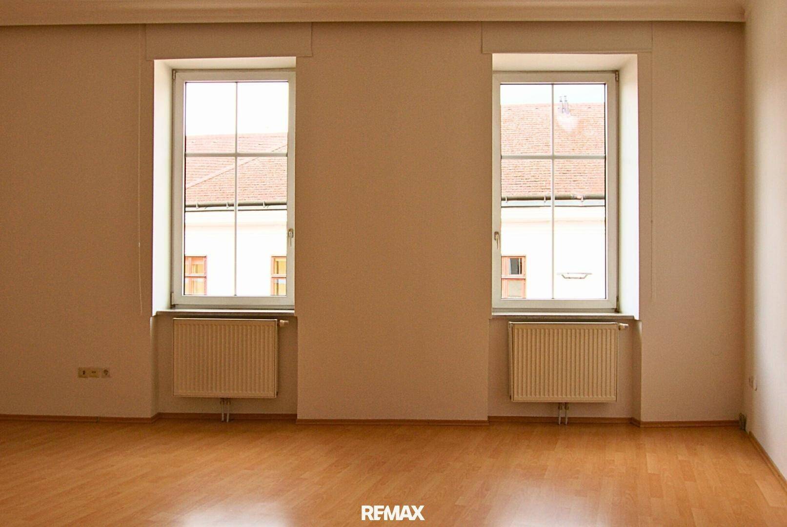 Heller Raum mit Holzboden und zwei Fenstern, die viel Tageslicht hereinlassen.