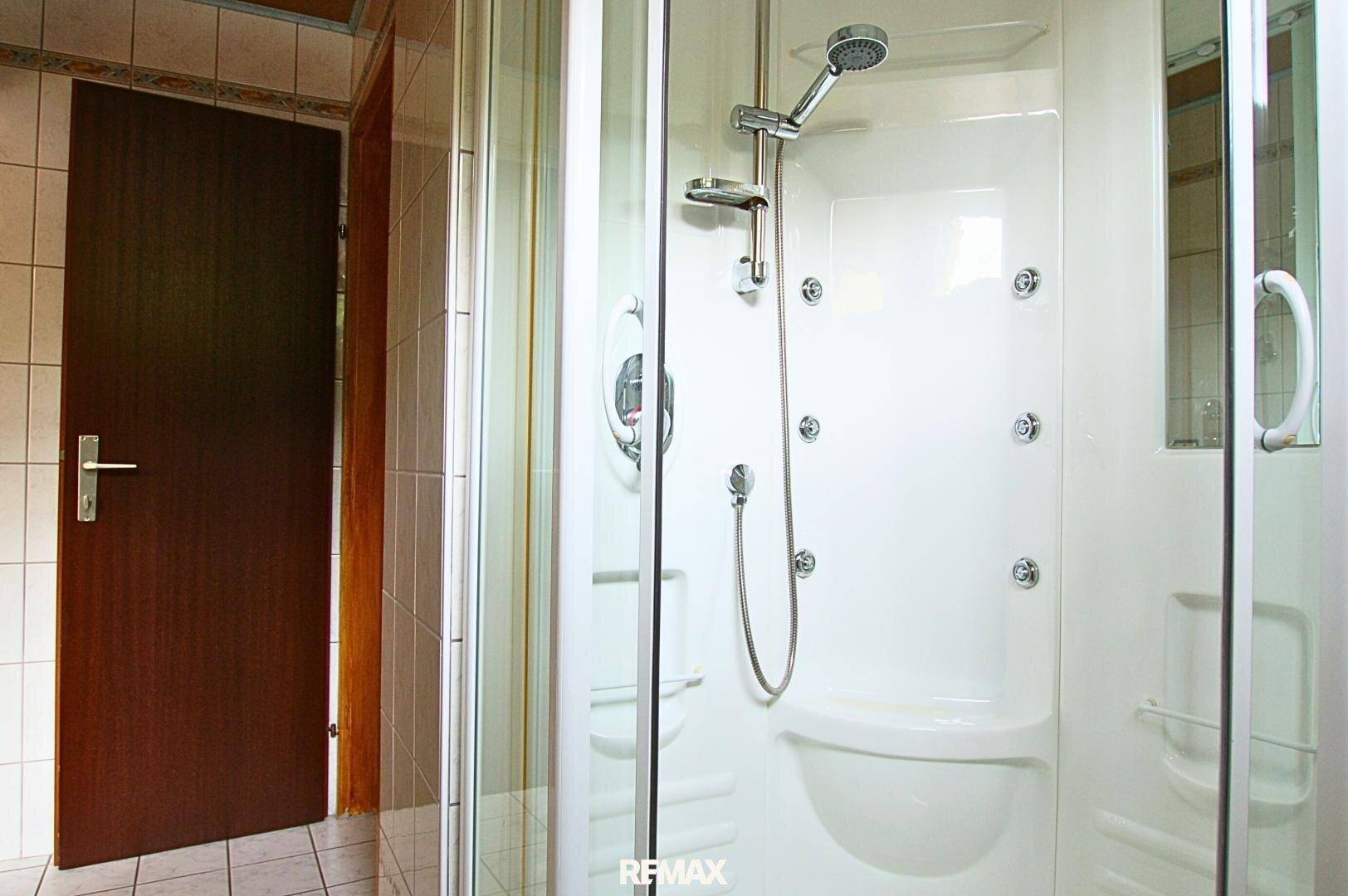 Moderne Duschkabine mit mehreren Massagedüsen und Handbrause in einem gefliesten Badezimmer.