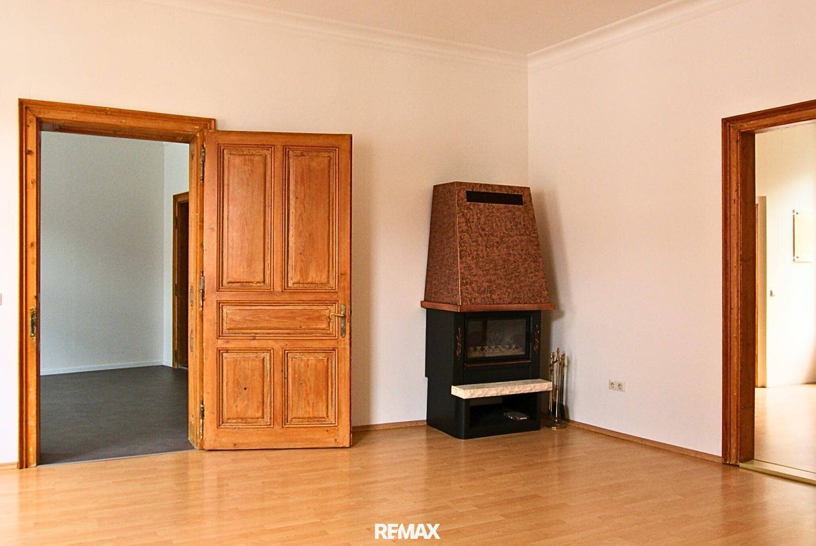 Geräumiges Wohnzimmer mit hellem Holzboden, Kamin und traditionellen Holztüren.