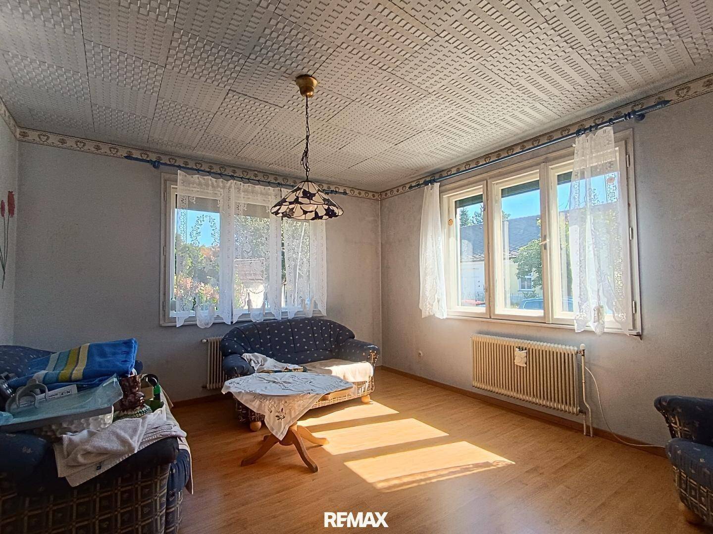 Gemütliches Wohnzimmer mit gemusterter Tapete, Holzboden und viel natürlichem Licht durch die Fenster.