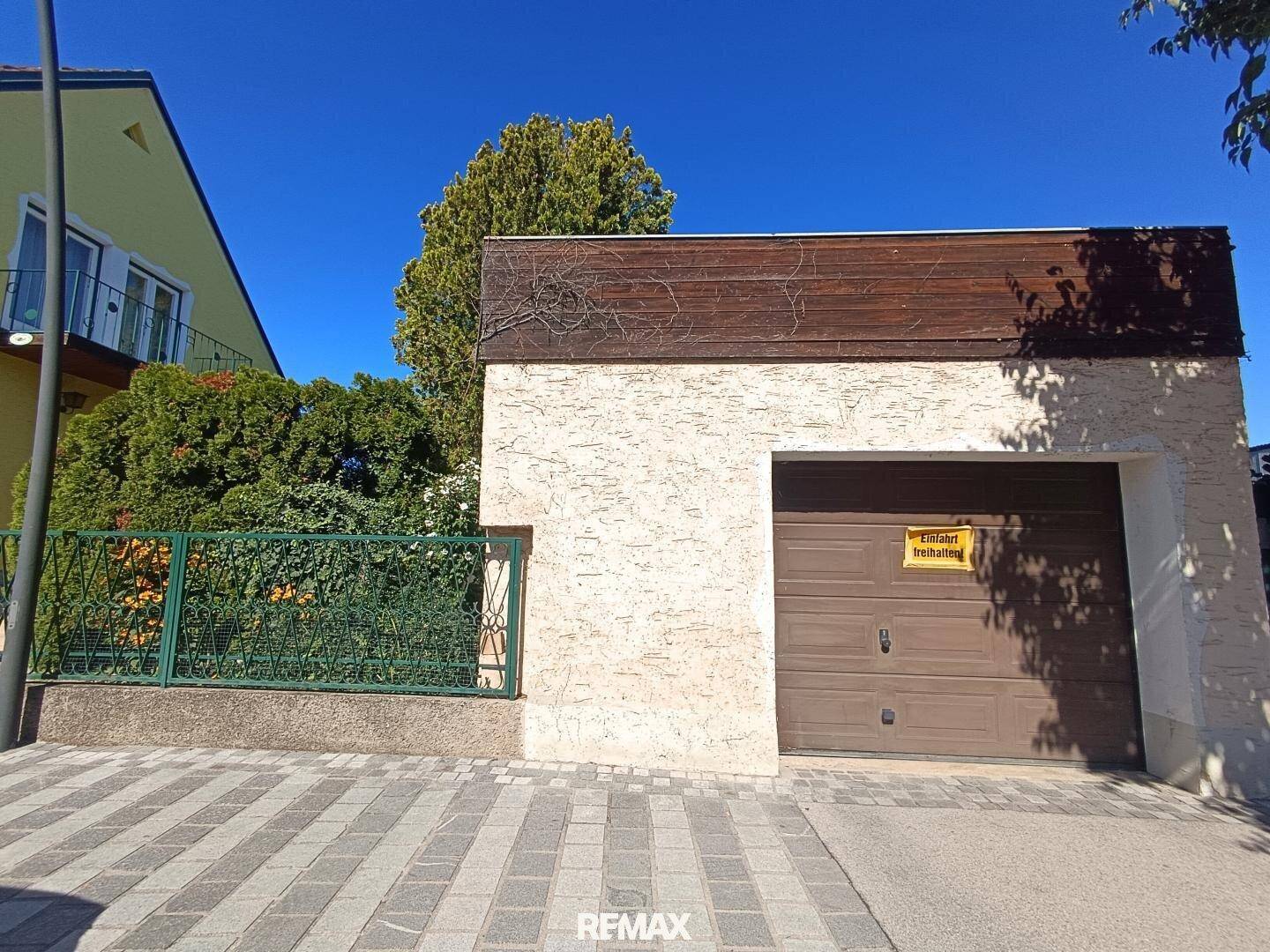 Garage mit braunem Tor und strukturierter Fassade, davor ein gepflasterter Bereich.