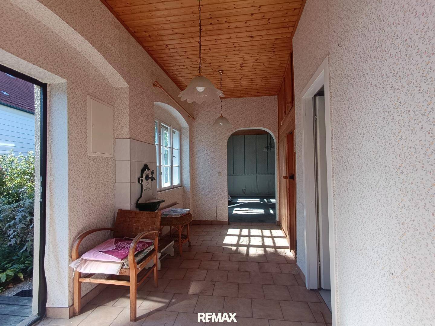 Heller Eingangsbereich mit Fliesenboden, Holzdecke und natürlichem Lichteinfall durch ein Fenster.