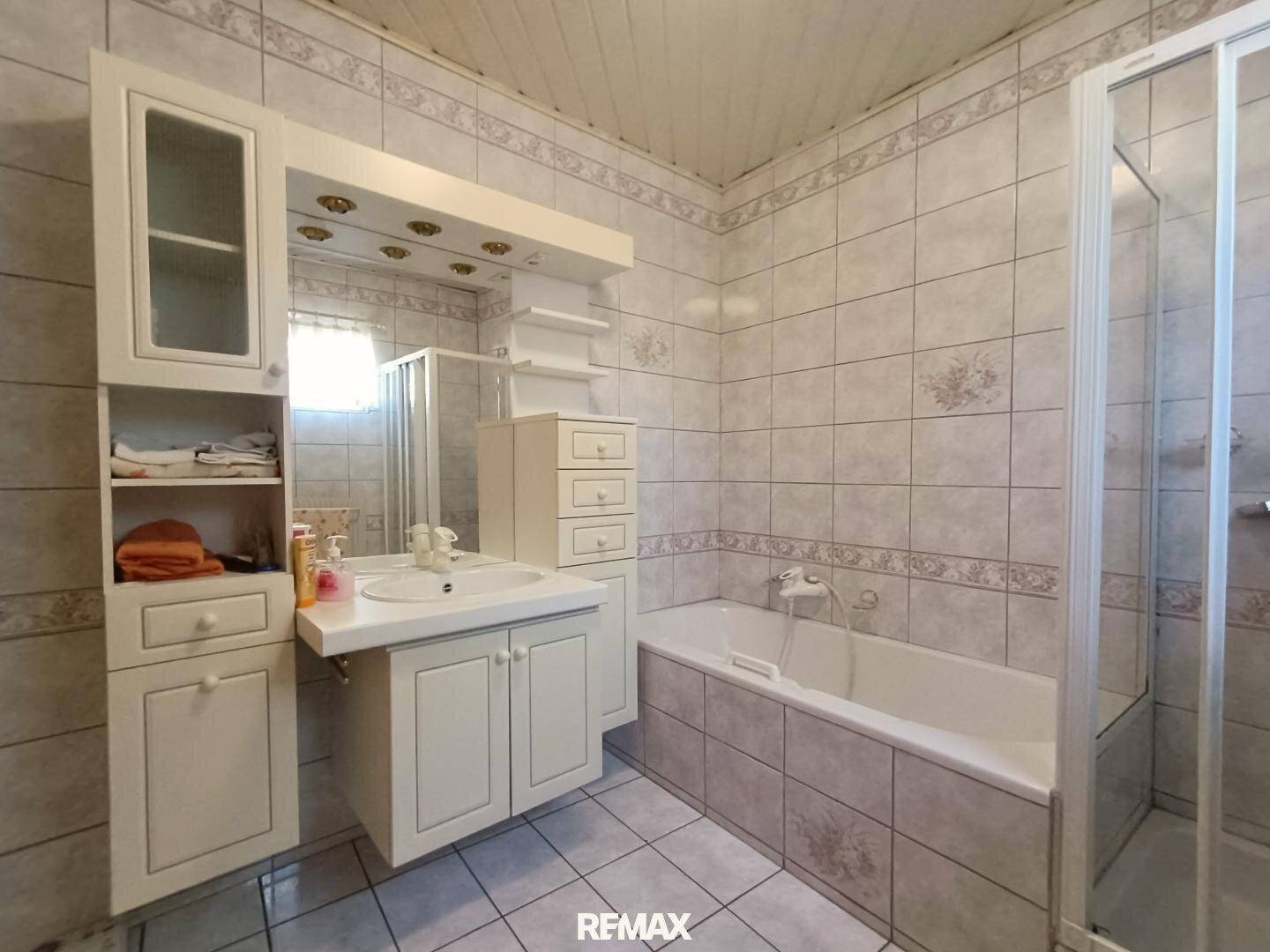 Helles Badezimmer im Stil der 80er Jahre mit Badewanne, Dusche und weißer Waschtischkombination.