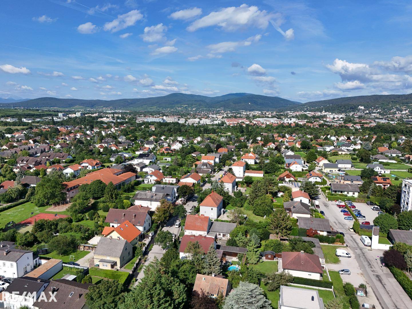 Weitläufige Luftaufnahme einer Wohnsiedlung mit vielen Häusern und Bergen im Hintergrund.