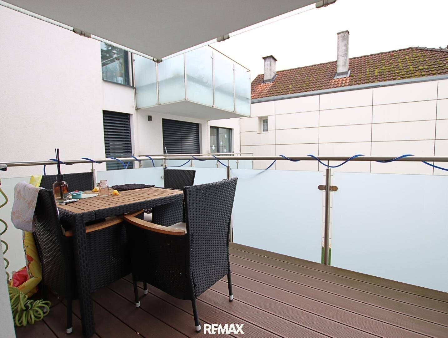 Möblierter Balkon mit Holzboden und Glasgeländer, ideal für entspannte Stunden im Freien.