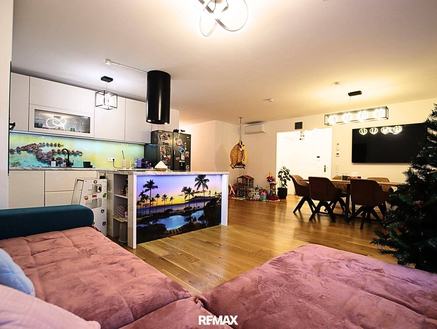 Gemütlicher Wohnbereich mit Sofa und Blick auf die moderne Küche mit dekorativer Rückwand.