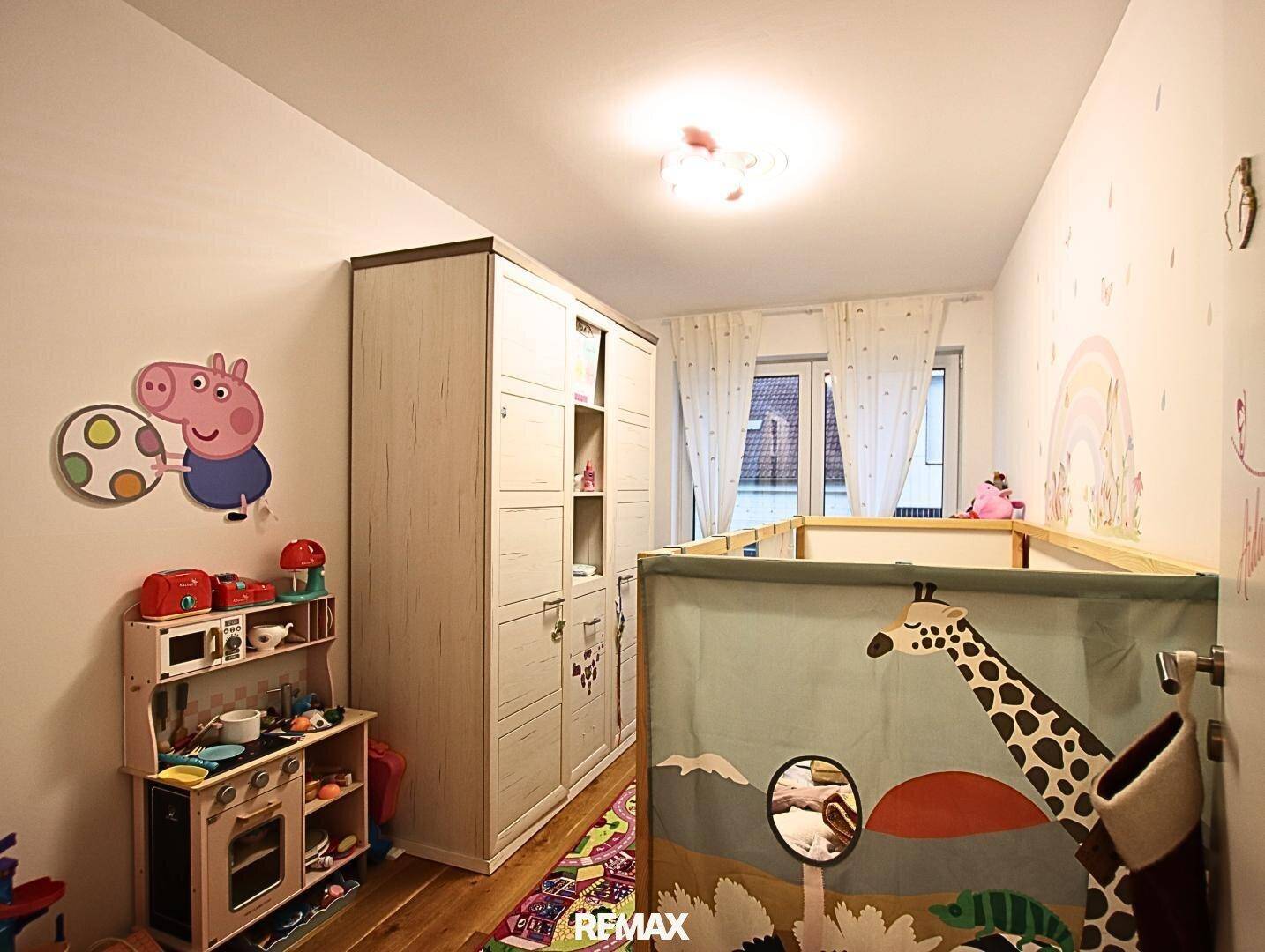 Kinderzimmer mit Spielbereich, Kleiderschrank und farbenfrohen Wanddekorationen.