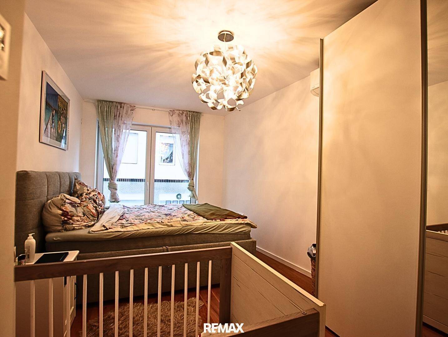Schlafzimmer mit Doppelbett und Babybett, helle Atmosphäre und Zugang zum Balkon.