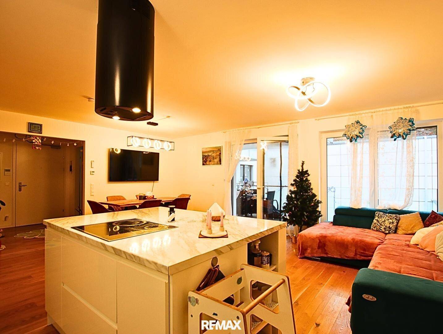 Moderne Kücheninsel mit Induktionskochfeld im offenen Wohnbereich mit Sofa und Balkonzugang.