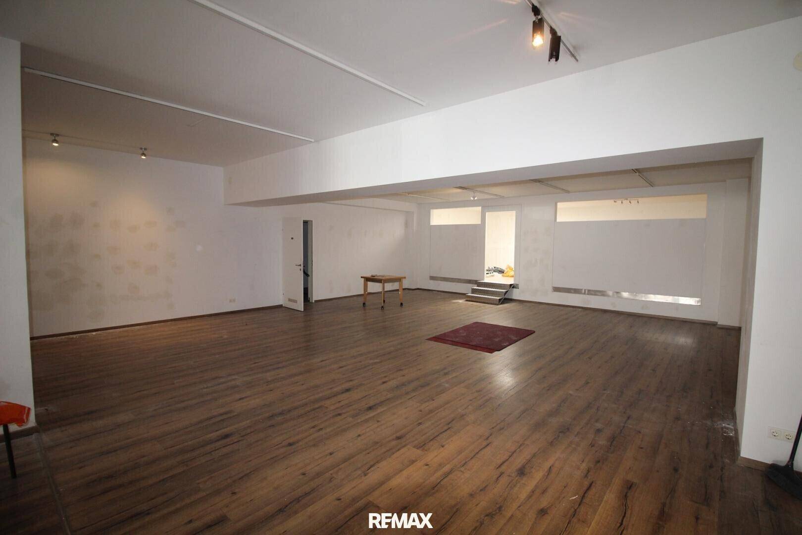 Großer, leerer Raum mit Laminatboden und hohen Decken, ideal für gewerbliche Nutzung.