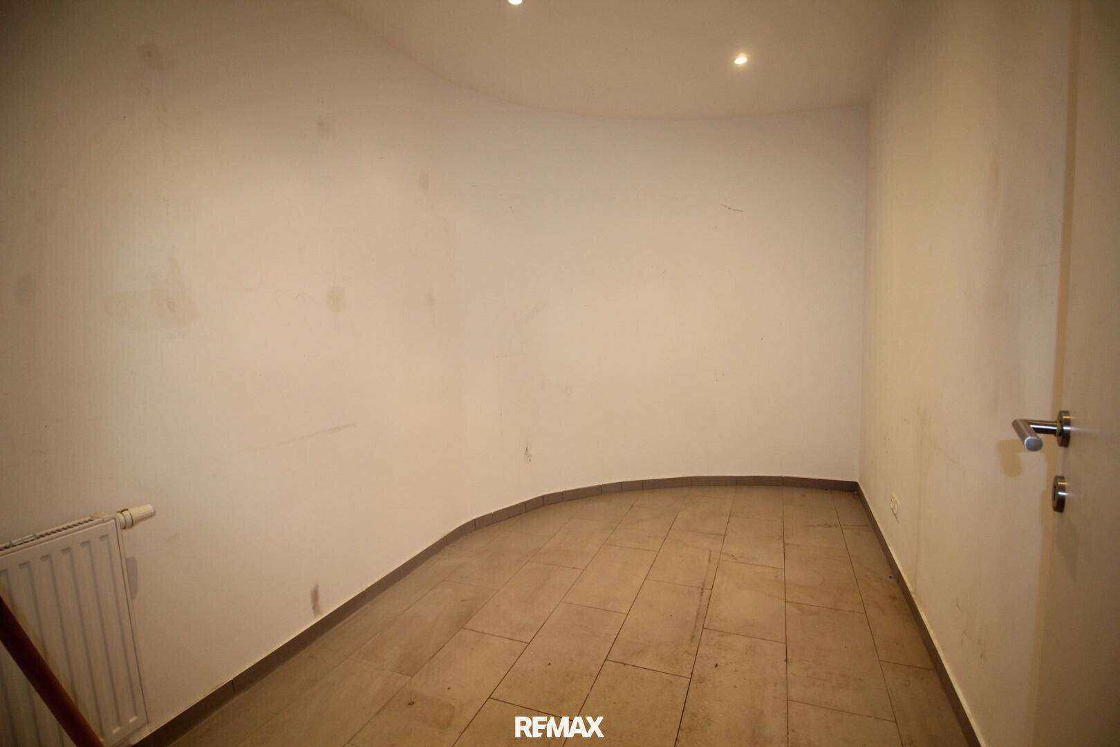 Leerer Raum mit einer geschwungenen Wand, Heizkörper und Fliesenboden.