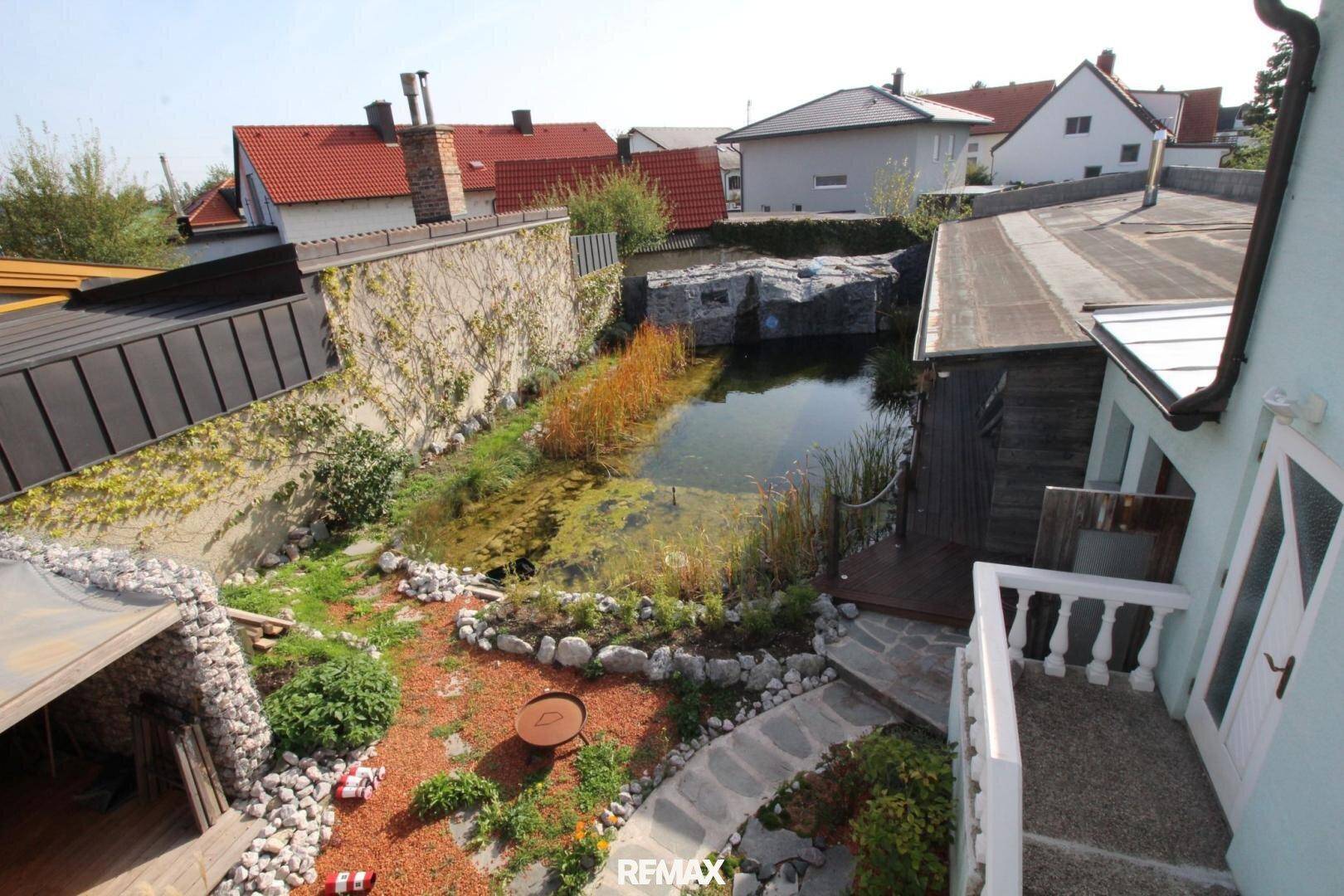 Gartenanlage mit Teich, Steinpfad und Blick auf die umliegenden Wohnhäuser.