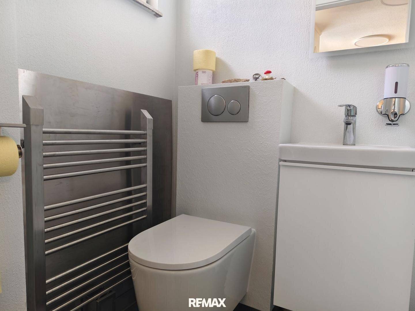 Modernes WC mit wandhängender Toilette, Waschbecken und beheiztem Handtuchhalter.