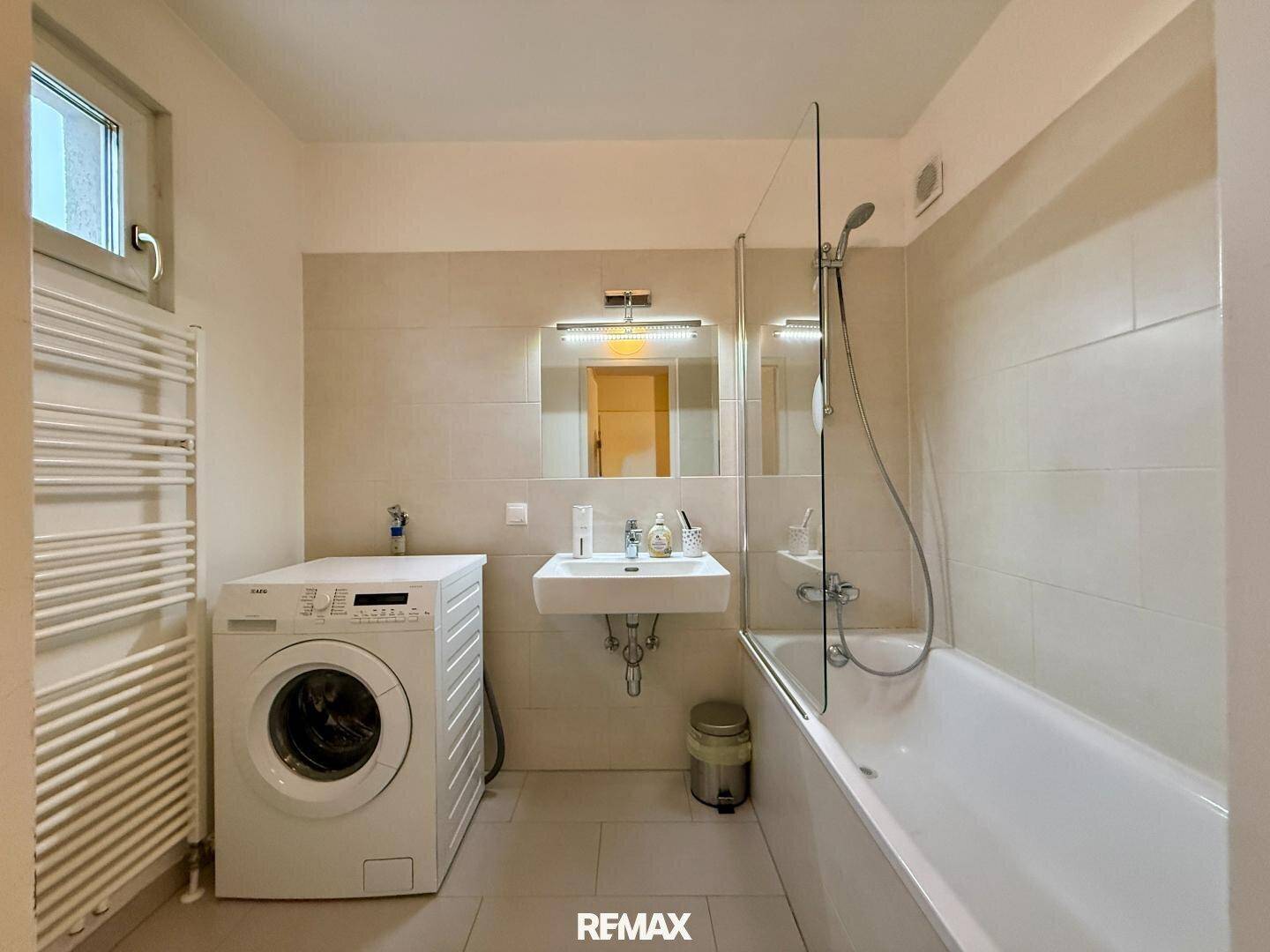 Helles Badezimmer mit Badewanne, Duschabtrennung, Waschbecken und Waschmaschine.