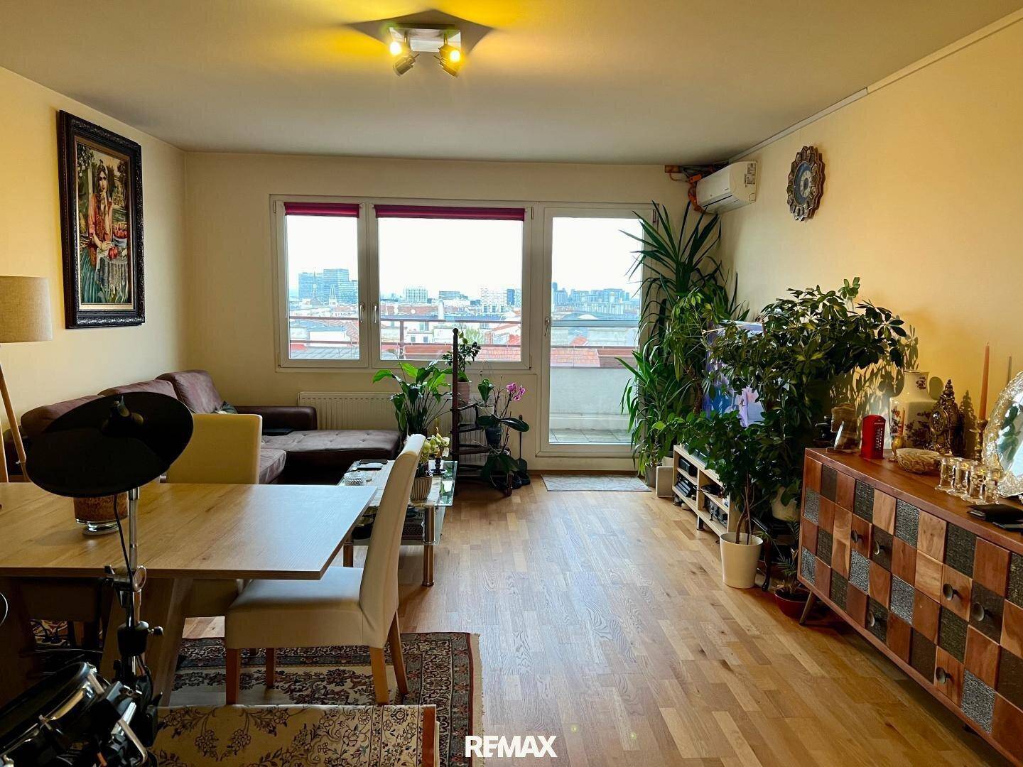 Geräumiger Wohn-Essbereich mit Holzboden, bequemer Couch und Zugang zu einem Balkon mit Stadtblick.