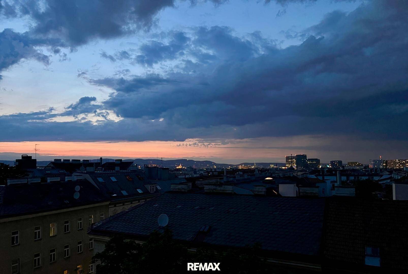 Panoramablick über die Stadt bei Sonnenuntergang mit beleuchteten Gebäuden und dramatischem Himmel.