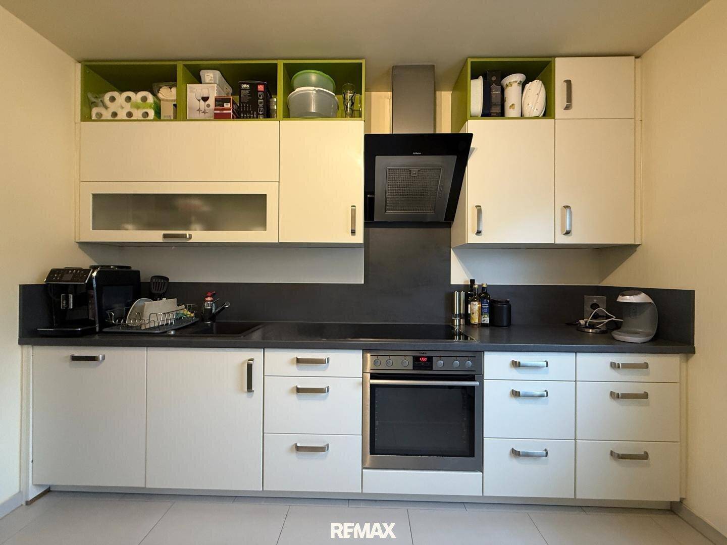 Moderne Einbauküche mit weißen und grünen Schränken, integriertem Backofen und Dunstabzugshaube.