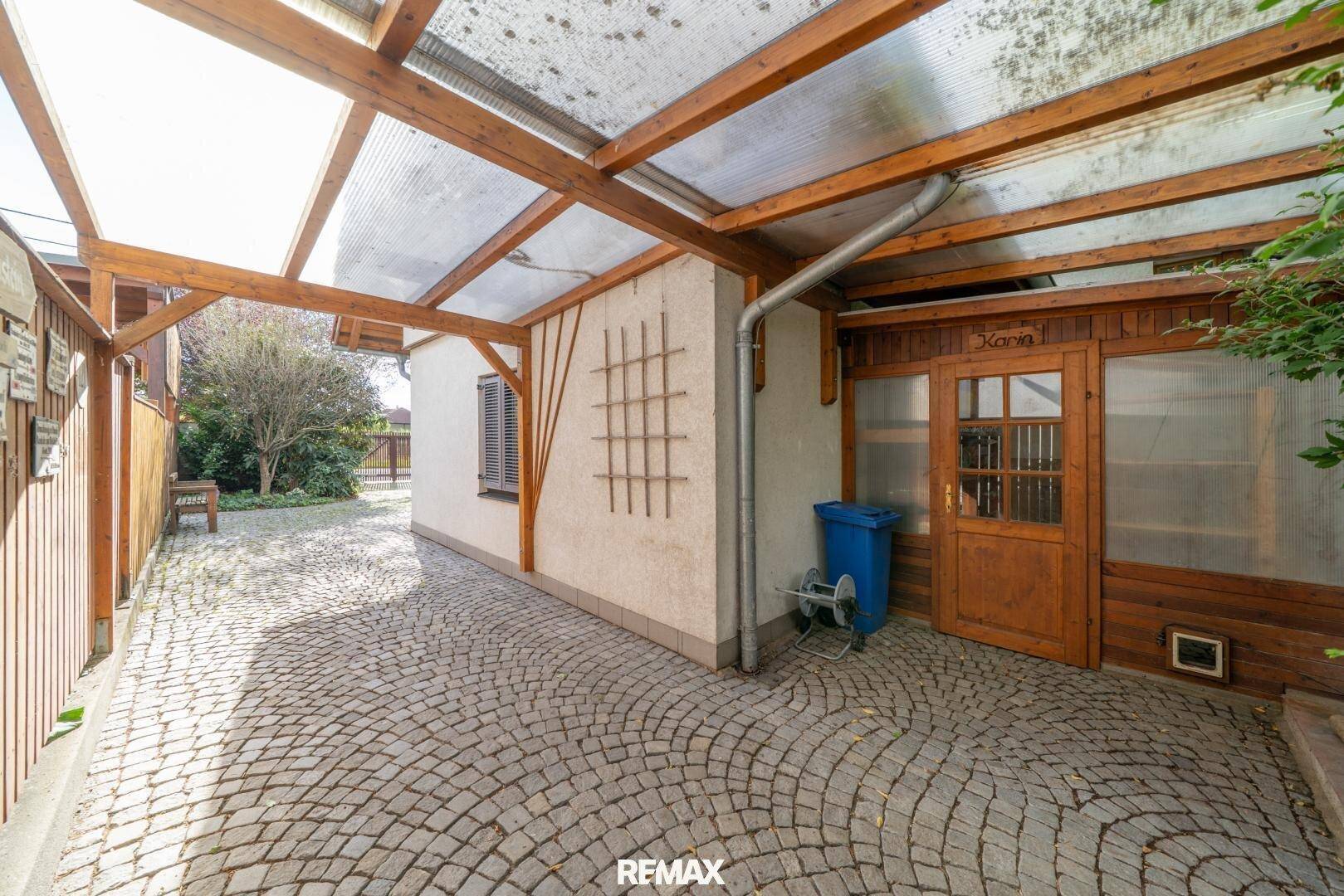 Überdachter Carport-Bereich mit Kopfsteinpflaster und Holzelementen.