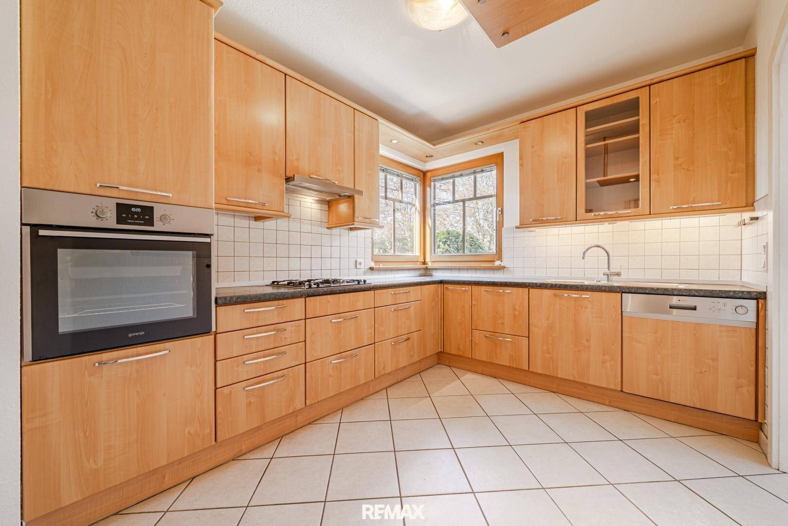 Funktionale Küche mit hellen Holzschränken, Fliesenrückwand und eingebauten Geräten.
