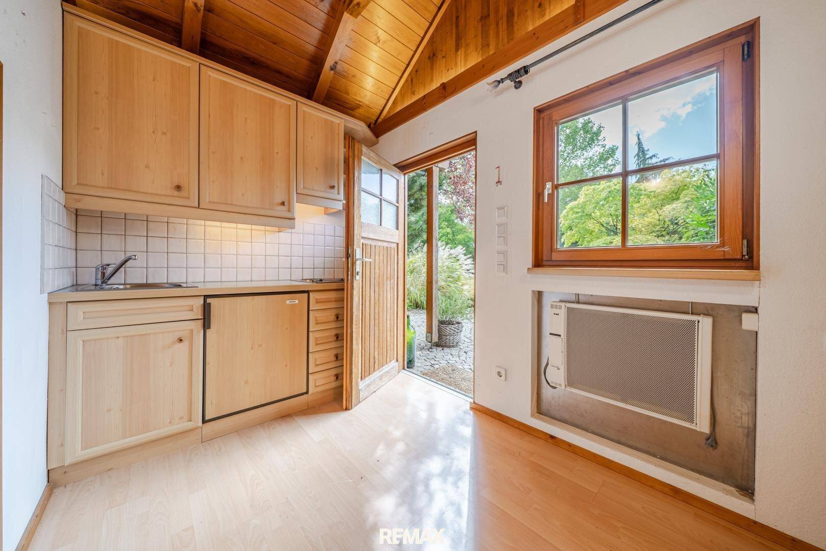 Kleine Küchenzeile mit Holzschränken, Spüle und Zugang zum Gartenbereich.