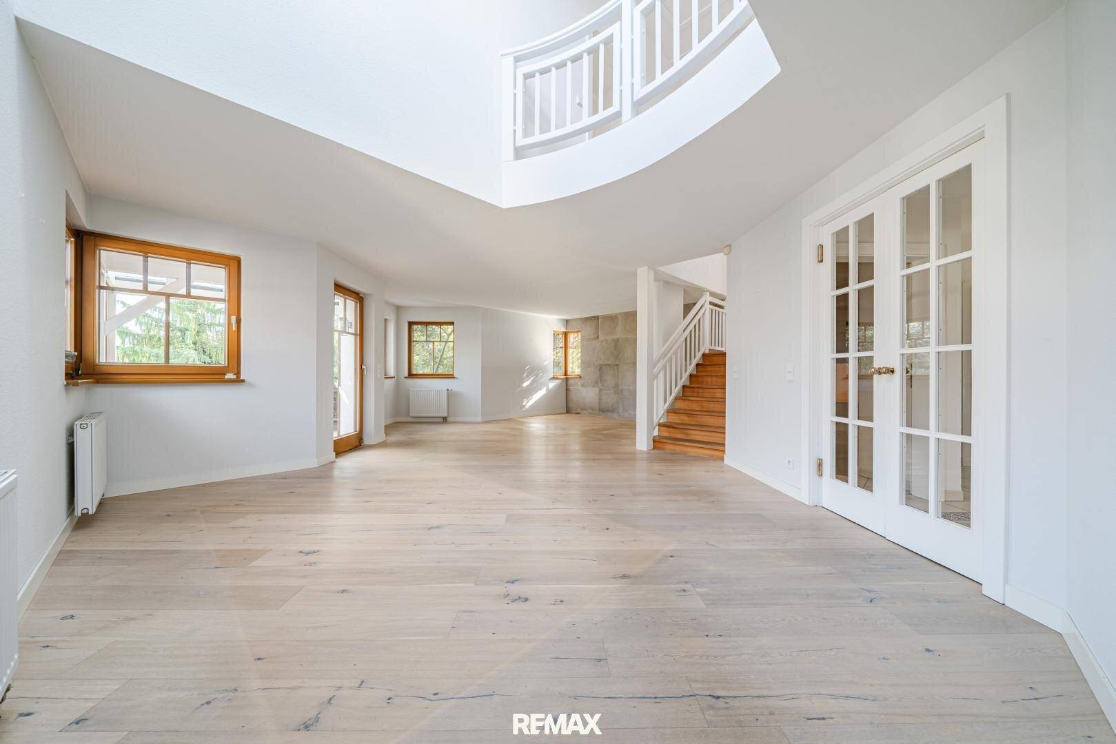 Helles, offenes Wohnzimmer mit Holzboden, geschwungener Treppe und viel Tageslicht.
