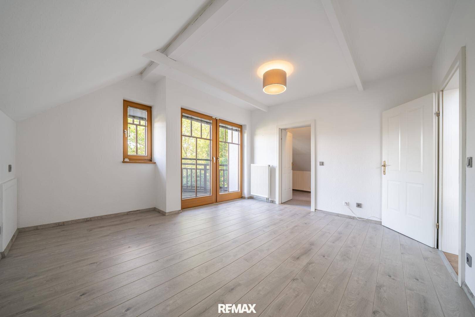 Geräumiges Schlafzimmer mit hellem Holzboden, Fenster und Zugang zu einem französischen Balkon.