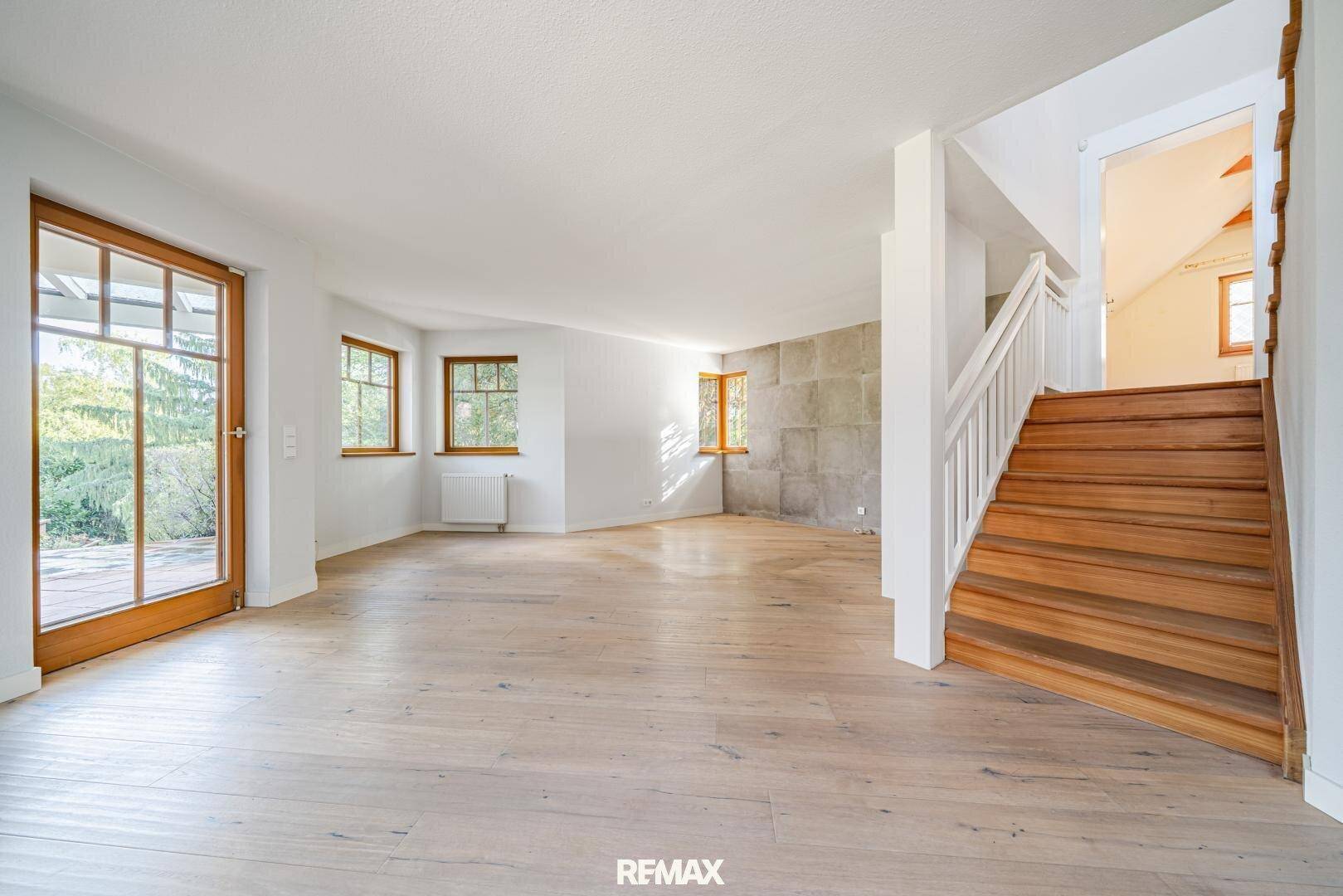 Geräumiger, heller Raum mit Holzboden, vielen Fenstern und einer Holztreppe.