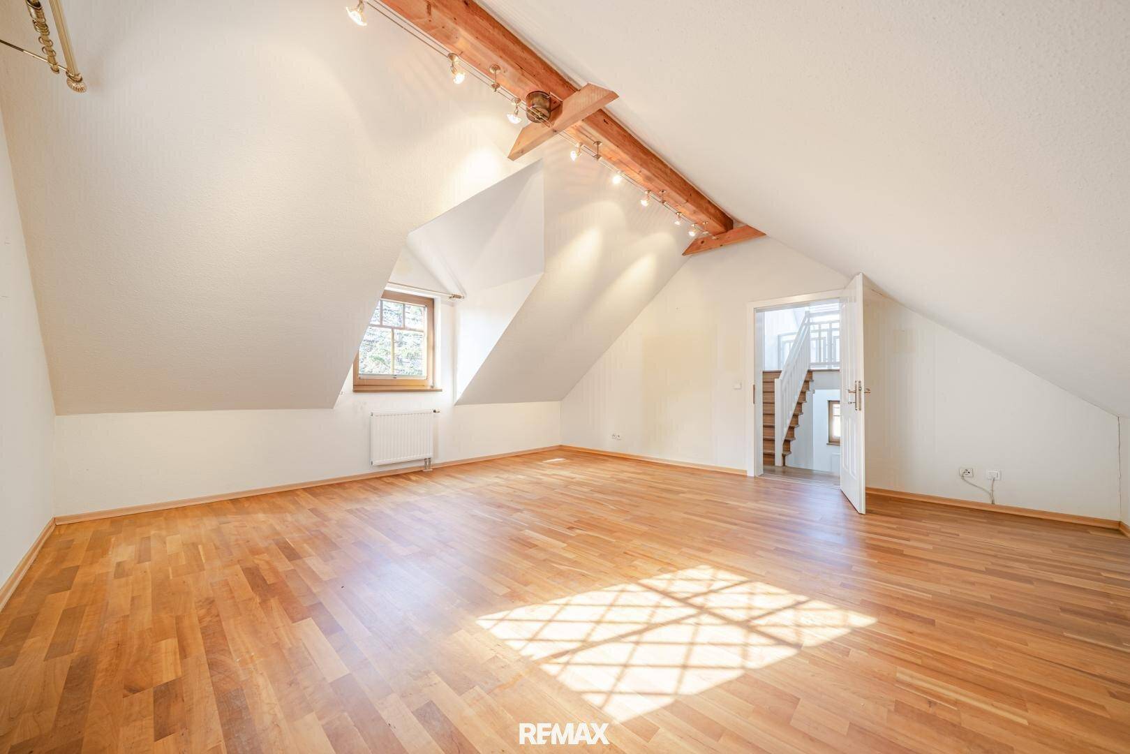 Helles Dachzimmer mit schrägen Decken, sichtbaren Holzbalken und Holzboden.