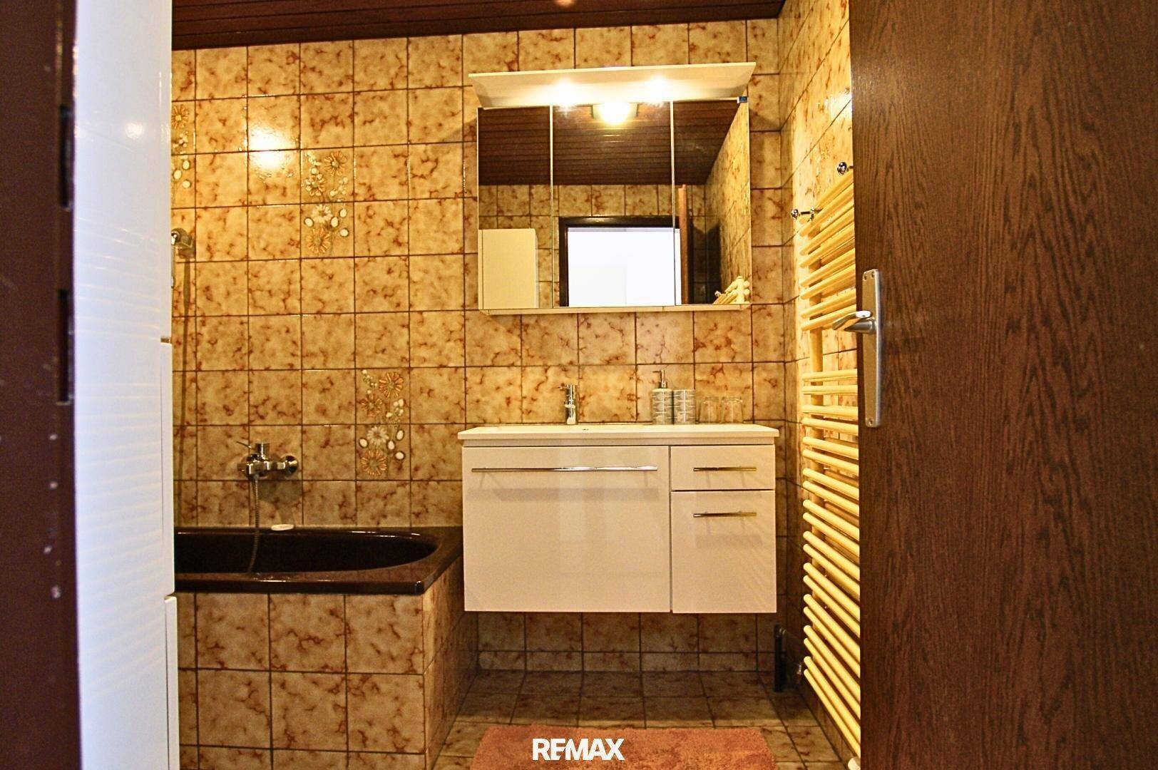 Badezimmer mit braunen Fliesen, Badewanne und einem modernen Waschtisch mit Spiegelschrank.
