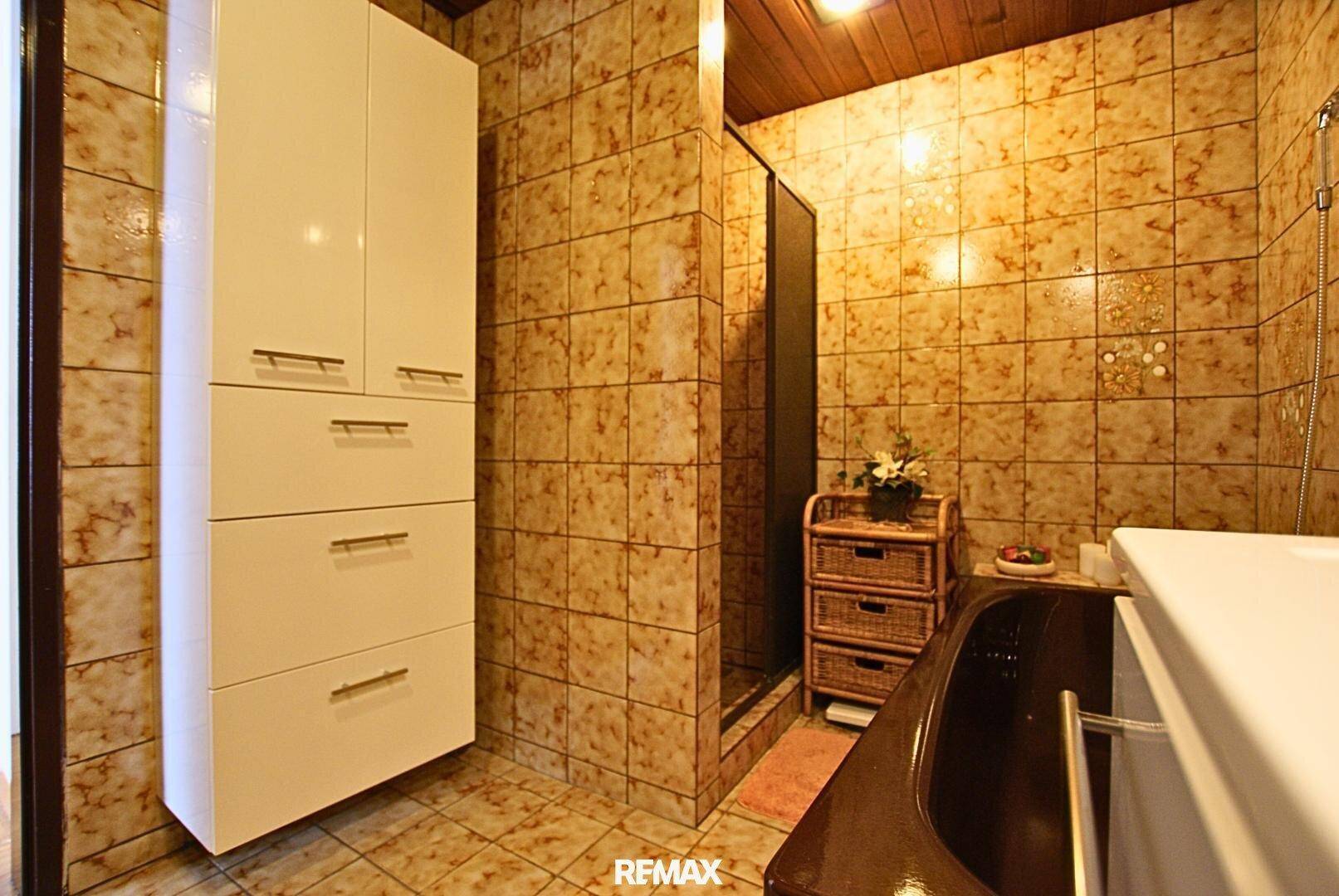 Badezimmer mit braunen Fliesen, einer Dusche und einem modernen weißen Hochschrank.