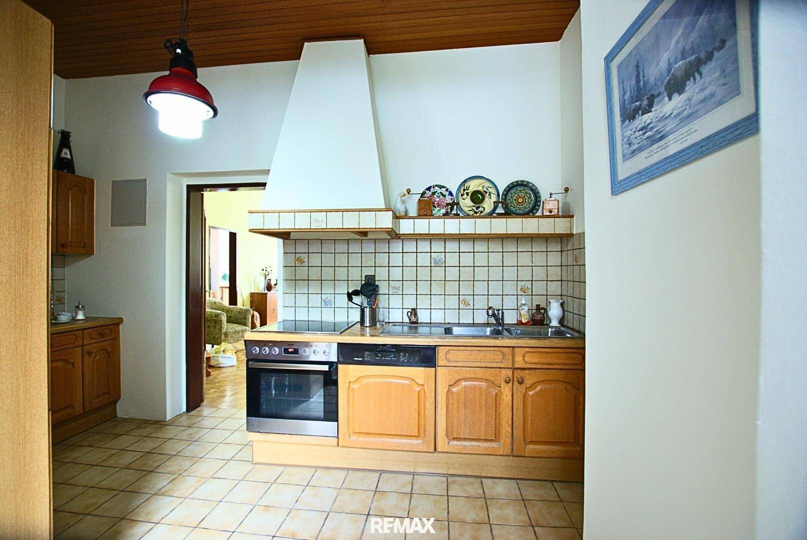 Funktionale Küche mit Holzschränken, Herd, Backofen, Geschirrspüler und Fliesenboden.
