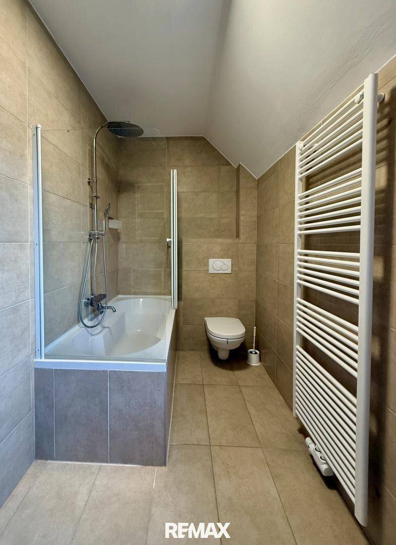 Badezimmer mit Badewanne, integrierter Dusche, WC und beheiztem Handtuchhalter.