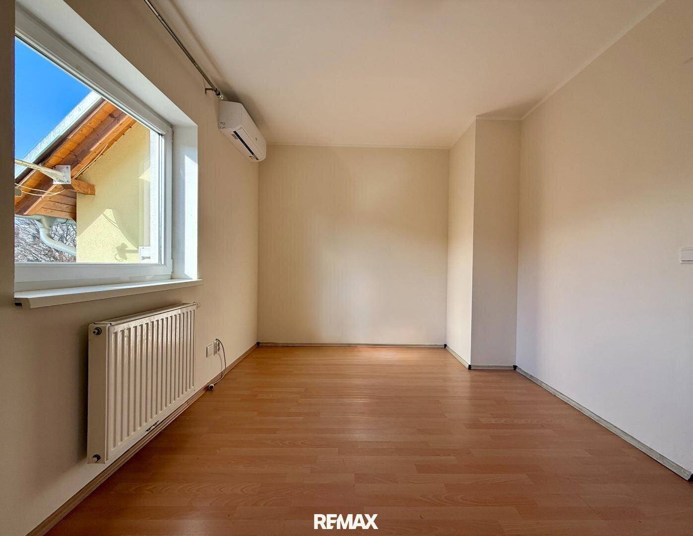Helles Schlafzimmer mit Holzboden, Heizkörper und Klimaanlage unter dem Fenster.