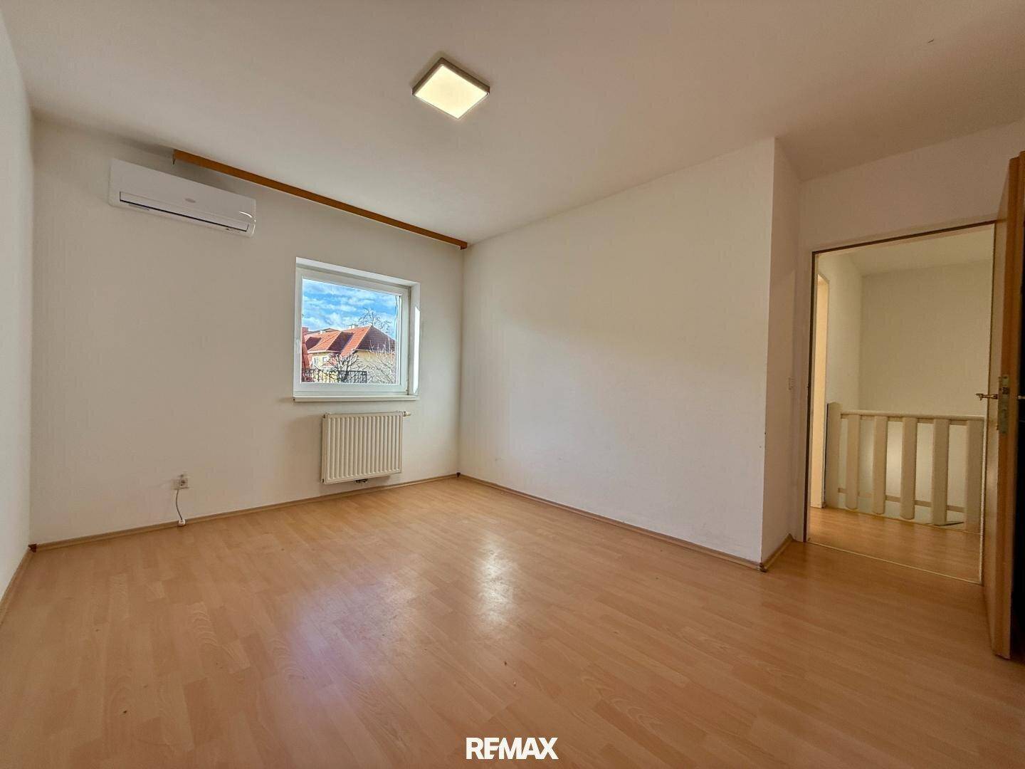Leeres Schlafzimmer mit Holzboden, Fenster und Klimaanlage, Blick auf die Umgebung.
