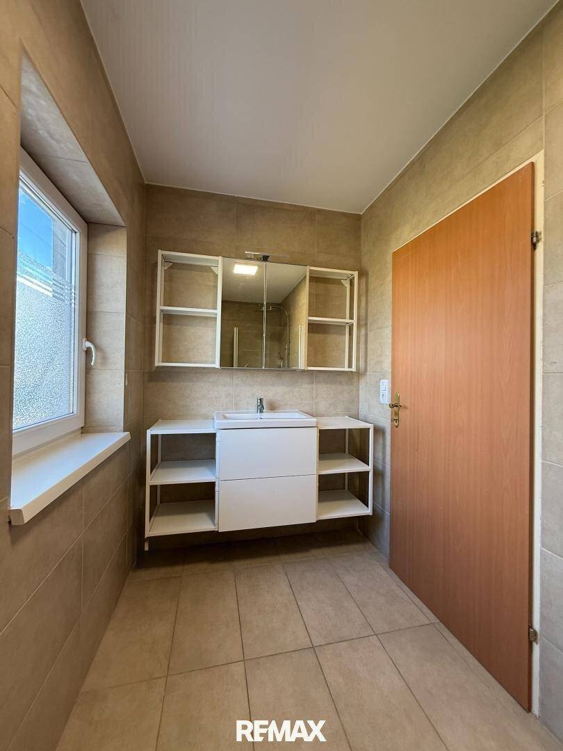 Geräumiges Badezimmer mit beigefarbenen Fliesen, großem Waschtisch und Fenster.