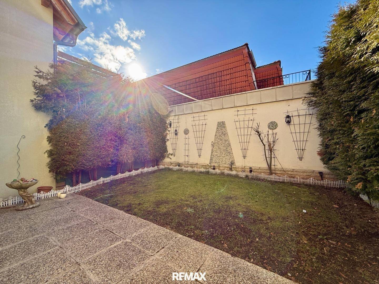 Kleiner, gepflegter Gartenbereich mit Rasenfläche, Terrasse und Heckenbegrenzung.