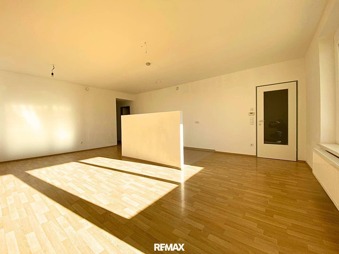 Heller, leerer Wohnraum mit Parkettboden und viel natürlichem Licht durch große Fenster.