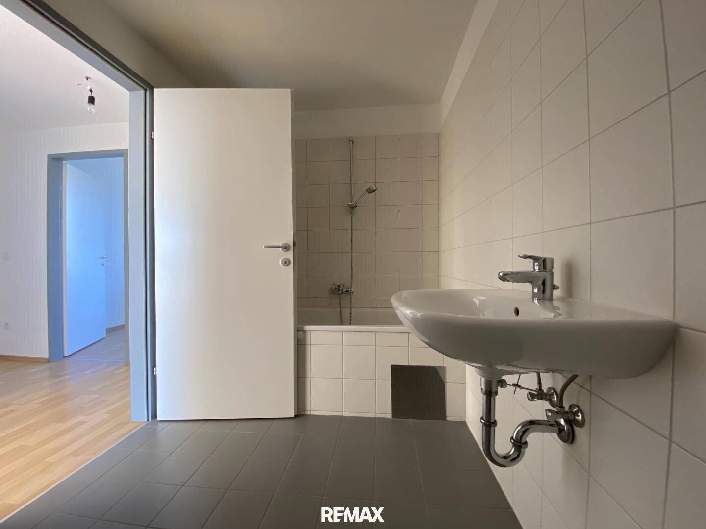Funktionales Badezimmer mit Badewanne, Waschbecken und hellen Fliesen, bereit zur individuellen Gestaltung.