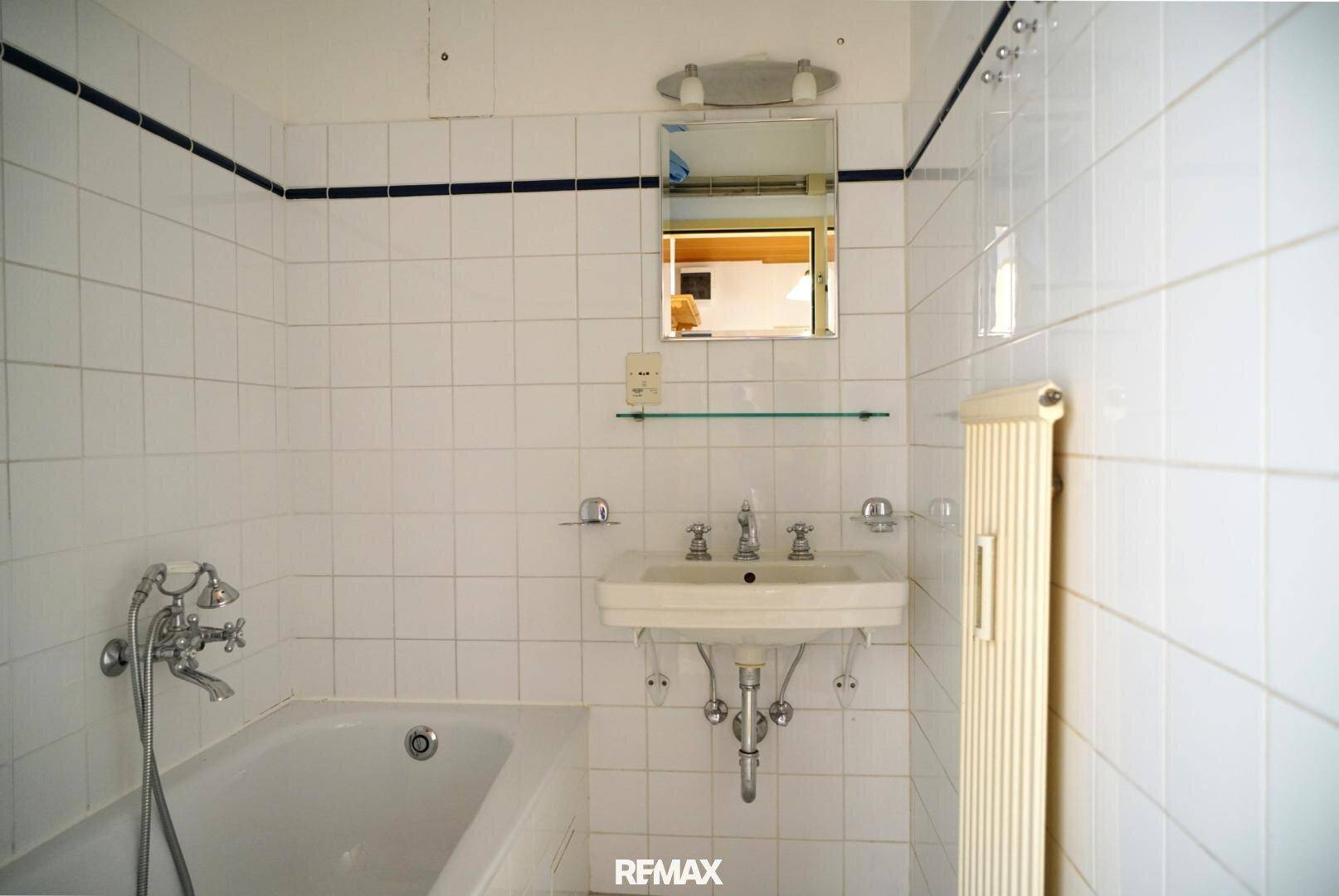 Badezimmer mit Badewanne, Waschbecken und weißen Fliesen im 80er-Jahre-Stil, funktional.