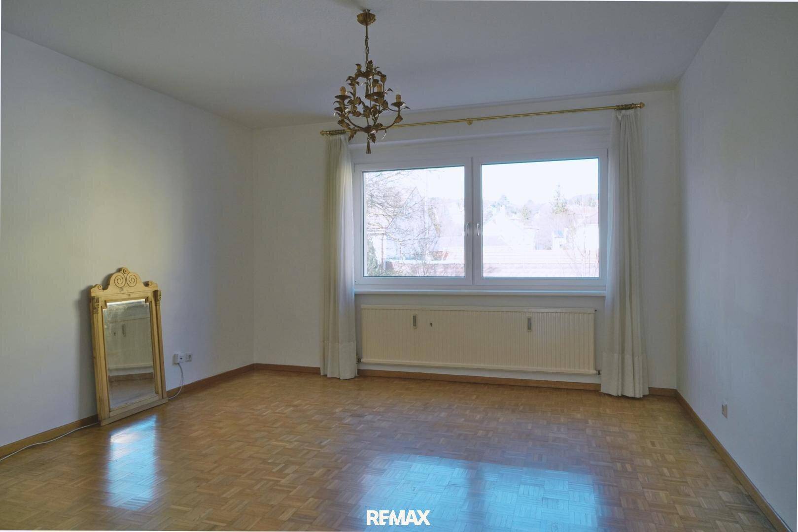 Leeres Schlafzimmer mit Parkettboden, großem Fenster und viel Tageslicht, unmöbliert.