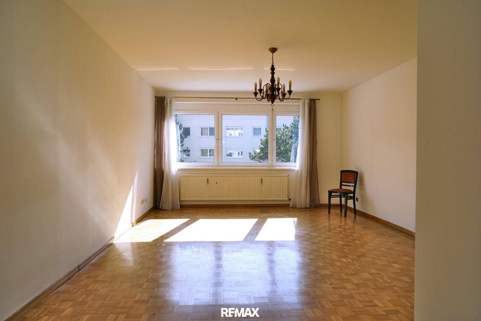 Leeres Wohnzimmer mit Parkettboden, großem Fenster und viel Tageslicht, bereit zur Einrichtung.